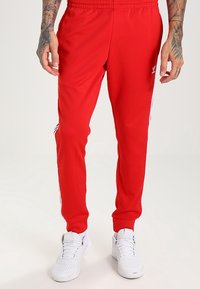 Röda sportbyxor med en texturerad tyg, med vita sidostreks. Midjan är elastisk och vita sneakers används.