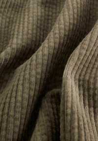 Tissu marron côtelé avec une texture douce, présentant des rayures alternées claires et foncées, des plis créant de la profondeur et un intérêt visuel.