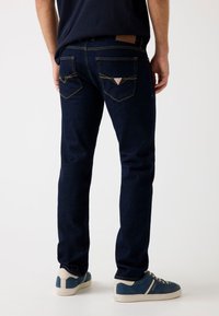 Jeans in denim blu scuro con un design aderente, cuciture gialle a contrasto e due tasche posteriori con un dettaglio a logo triangolare.