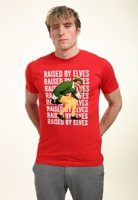 Červené bavlněné tričko s bílým nápisem "RAISED BY ELVES" a grafikou elfa v zeleném oblečení a žlutých punčochách.