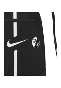 Zwarte trekkoordtas gemaakt van duurzaam materiaal. Voorzien van een wit Nike-logo en een rond zwart-wit Freiburg-embleem. Horizontale streepdetails.