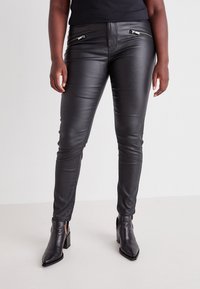 Black faux leather pants with two zippered front pockets, fitted design, and stitched details along the legs, paired with black ankle boots.