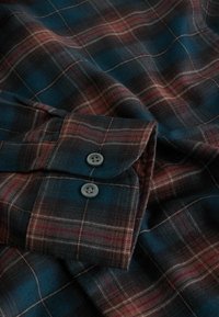 Chemise en flanelle avec un motif à carreaux bleu, marron et rouge. Dotée d'un poignet à bouton en tissu doux et texturé.