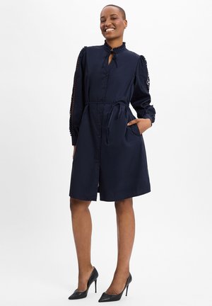 Marineblaues Hemdblusenkleid mit Kragen, langen Ärmeln mit Haardetails, Taillengürtel und Seitentaschen. Glatter Stoff, knielanges Design.