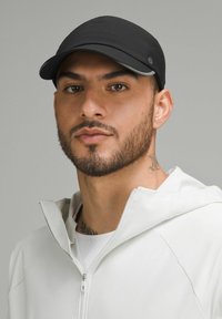 Gorra negra con superficie texturizada, visera curva y logo bordado, combinada con una chaqueta blanca con cremallera y una capa base con estampado.