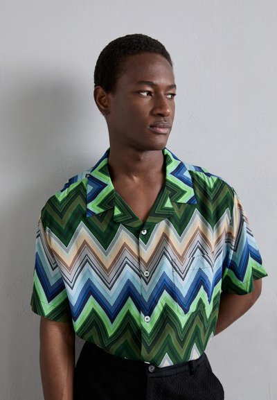 Chemise à manches courtes avec un motif en zigzag dans des nuances de vert, bleu et beige. Fabriquée en tissu léger avec un col et des boutons.