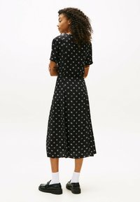 Abito nero con maniche corte, stampa floreale bianca, lunghezza al ginocchio, scollatura rotonda e tessuto fluido. Indossato con scarpe nere e calzini bianchi.