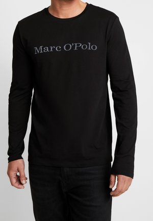 Mand iført en sort langærmet skjorte med teksten "Marc O'Polo" trykt i gråt henover brystet.