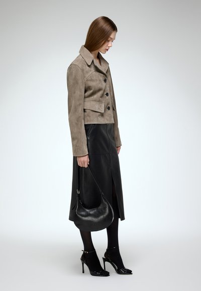 Cropped taupe suede jacket with black buttons; paired with a black leather skirt, black sheer tights, and high-heeled black sandals.