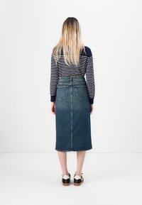 Denim midi svārki ar aizmugures kabatām, zilā krāsā, neapstrādāts maliņas apdare, kombinēti ar melniem un baltiem apaviem, un jūras zila svītrainā krekla ar garām piedurknēm.