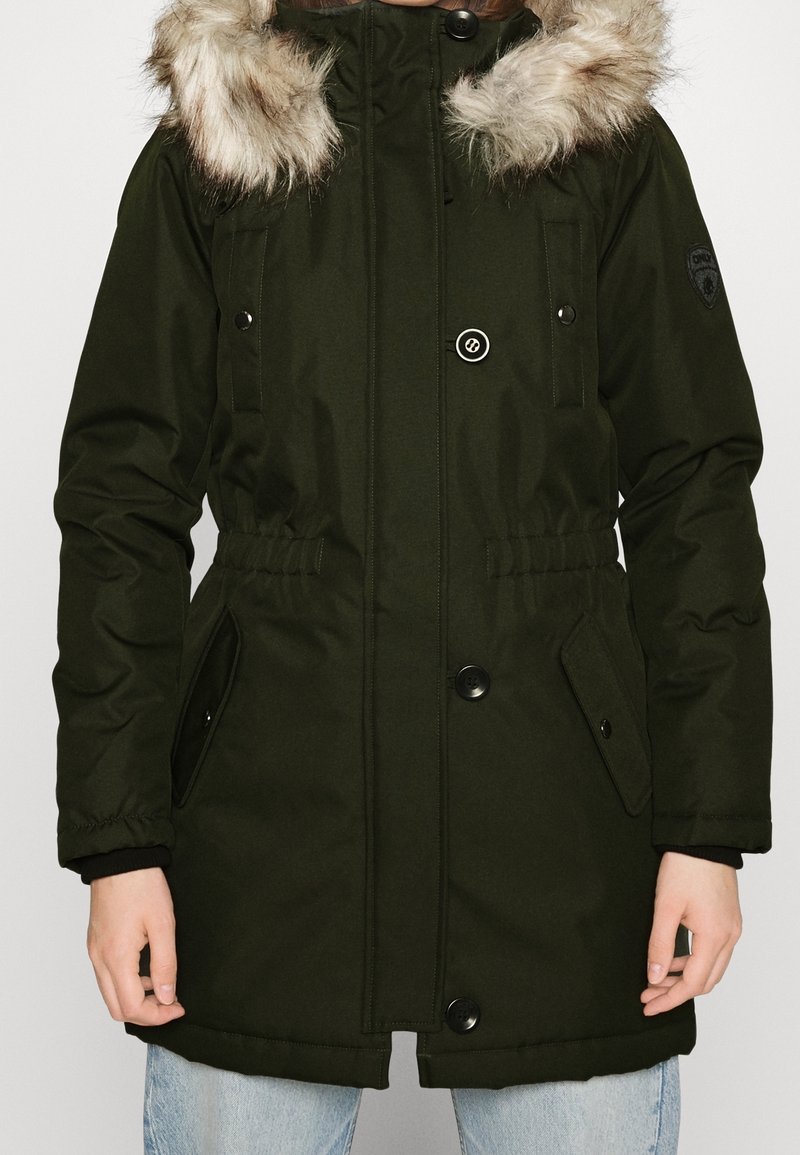 Parka vert foncé avec capuche doublée en fausse fourrure, fermetures à bouton, taille à cordon de serrage et poches latérales. Texture lisse, manches longues, design décontracté.