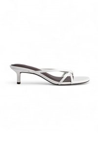 White heeled sandals with a cross-strap design, made of smooth material, featuring a slender heel and a textured dark footbed.