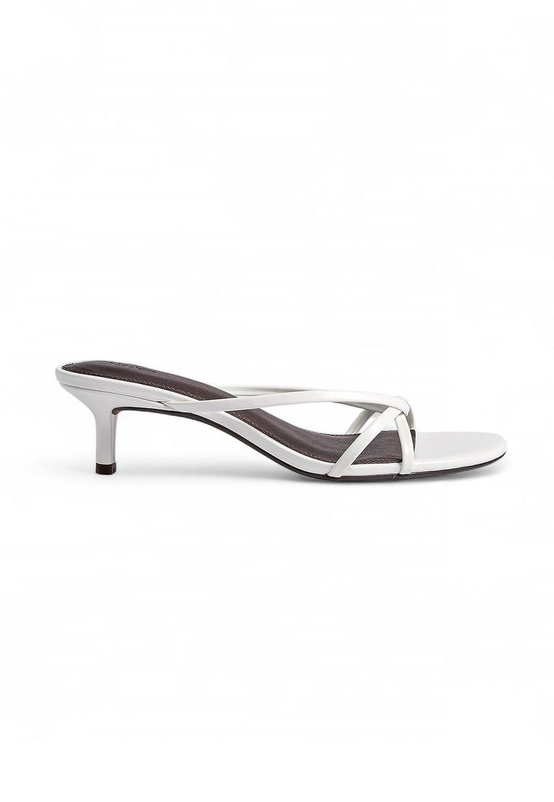 White heeled sandals with a cross-strap design, made of smooth material, featuring a slender heel and a textured dark footbed.