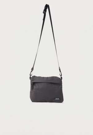 Geantă mică de umăr neagră, cu curea reglabilă, buzunar frontal cu fermoar și un patch discret cu logo-ul „TAION Mountain Wear” în partea dreaptă jos.