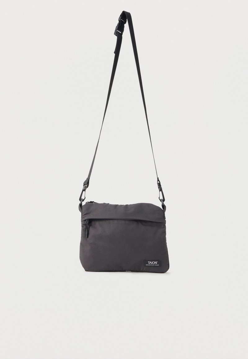 Μικρό μαύρο τσαντάκι ώμου με ρυθμιζόμενο ιμάντα, μπροστινή τσέπη με φερμουάρ και διακριτικό λογότυπο "TAION Mountain Wear" στο κάτω δεξιό μέρος.