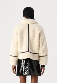 Kremfarget faux fur-jakke med bred krage, sort detaljer i borden og en løs passform. Kombinert med et svart skinnende miniskjørt.