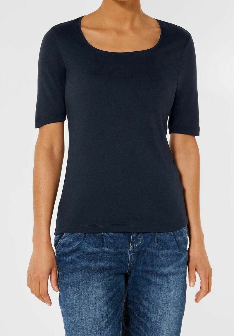 Femme portant un haut noir moulant à manches courtes avec un décolleté carré et un jean en denim bleu, vue du cou jusqu'aux hanches.