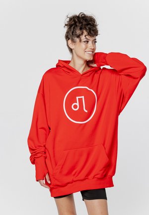 Czerwona, oversize bluza z kapturem, wykonana z miękkiego materiału. Posiada biały logo w okrągłym wzorze, kieszeń kangurzą oraz szerokie rękawy.