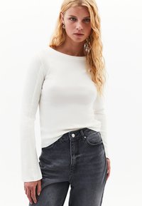 Vit långärmad topp med rund halsringning, kombinerad med högmidjade mörkgrå jeans. Mjuk tyg med subtil struktur.