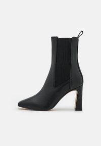 Bota de tobillo de cuero negro con puntera puntiaguda, paneles laterales elásticos y un tacón de bloque de 10 cm. Textura suave con un acabado mate.