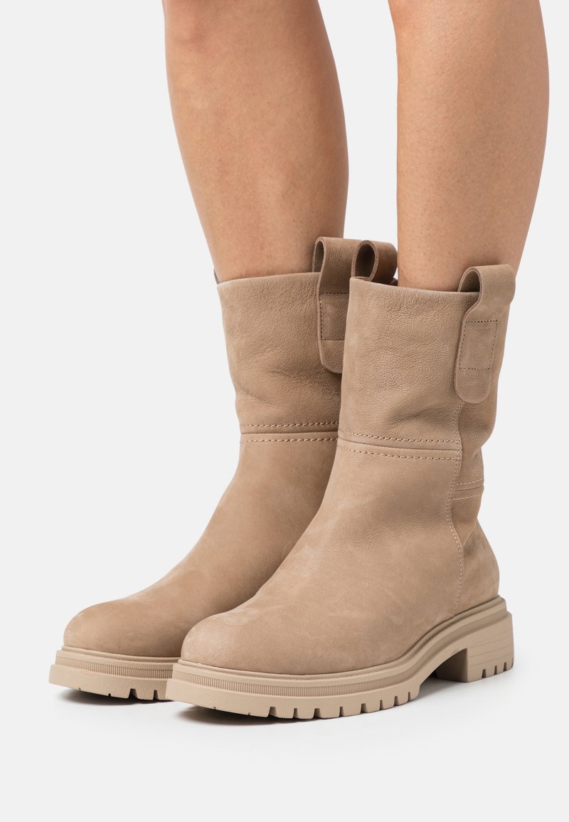 Bottines en suède beige avec un bout arrondi, des détails cousus et des onglets de traction, dotées d'une semelle épaisse et texturée pour une meilleure adhérence.