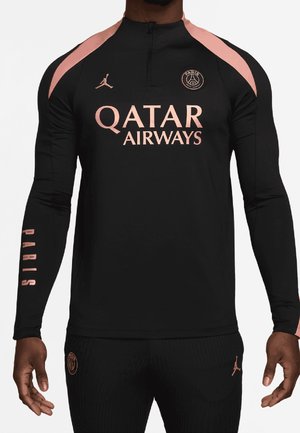 Mand iført sort og pink Paris Saint-Germain fodboldtrøje med Qatar Airways-logo og matchende sorte bukser.