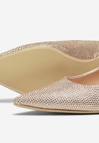 Ballerine a punta in oro rosa metallico con superficie testurizzata e borchiata. Suola beige con finitura liscia. Leggero luccichio dato dalle borchie.