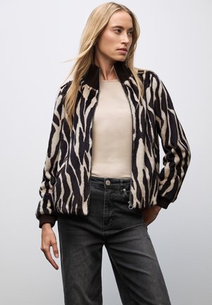Zebra-tijger gestreepte bomberjack in een wolmix, met een zwart en crèmewitte vormgeving, geribbelde manchetten en een ritsluiting. Gepaarde met donkere jeans.