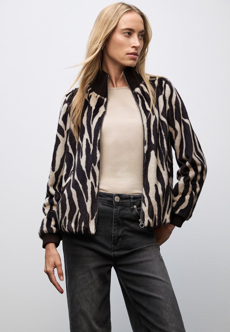 Veste bomber à motif zèbre en mélange de laine, avec un design noir et crème, des poignets côtelés et une fermeture éclair. Associée à un jean foncé.