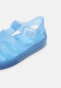 Transparent blue sandals with a chunky design, featuring a buckle strap and textured sole. Includes cut-out details for breathability.