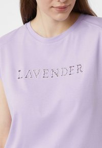 Kurzes Lavendel-Oberteil aus weicher Baumwolle, mit ausgeschnittenem Schriftzug, der "LAVENDER" in einem leicht dunkleren Lavendelton darstellt.
