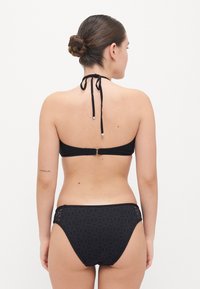 Črn bikini komplet z topom na halter vrat, ki se zapira s sponko, in visokim pasom z izrezanimi detajli. Gladka tekstura blaga.