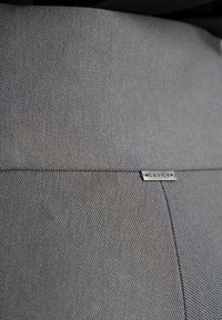 Szary materiał o teksturowanej powierzchni i detalu szwu. Do materiału przymocowana jest mała metalowa etykieta z napisem "CLICK".