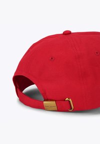 Cappellino da baseball in cotone rosso con visiera curva, cinturino regolabile e dettaglio in metallo dorato con il nome del marchio sul retro.