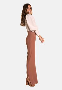 Blusa rosa claro con mangas abullonadas combinada con pantalones marrones de cintura alta con aberturas laterales, complementada con tacones de plataforma color beige.