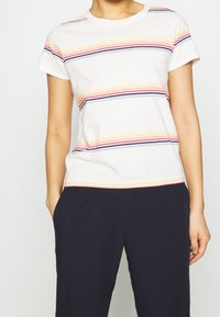 Kortærmet hvid T-shirt med multikolor vertikale striber i pink, gul og marineblå. Blødt bomuldsmateriale, klassisk crew neck stil.