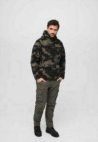 Fleece pullover with black, green, and blue camo pattern; half-zip neck; paired with olive cargo pants and black boots.