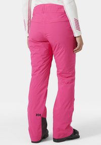 Růžové lyžařské kalhoty s texturou a vysokým pasem. Obsahují černé prvky a logo na dolní části nohy. Rovný střih.