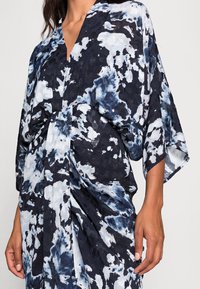 Kimonoklänning i marinblått och ljusblått batikmönster. Har V-ringning, lösa ärmar och insamling vid midjan. Mjuk tygstruktur.