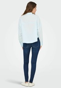 Light blue, long-sleeve shirt with a relaxed fit, worn with dark blue skinny jeans and white sneakers, viewed from the back.