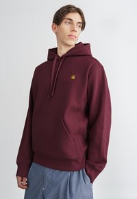 Bordo dukserica od mješavine pamuka s prednjim kengur džepom, kapuljačom s vezicom i izvezenim logotipom na prsima.