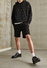 Black hooded sweatshirt and shorts with yellow smiley face patterns, paired with black lace-up shoes and white crew socks.