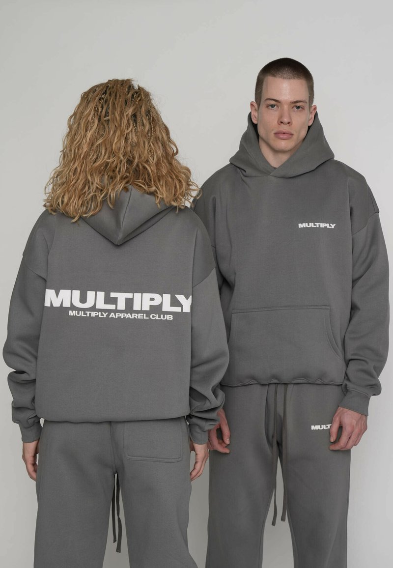 Las sudaderas con capucha grises presentan un gran logo "MULTIPLY" en la espalda y un logo más pequeño en la parte delantera. La tela parece suave y con textura.