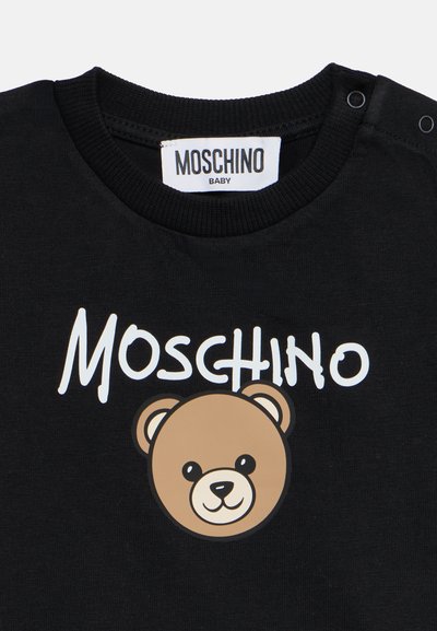 Μαύρο βρεφικό μπλουζάκι με λευκό κείμενο "Moschino" και ένα χαμογελαστό πρόσωπο αρκουδάκι κάτω από το κείμενο, με κουμπιά σούστες στον ώμο.