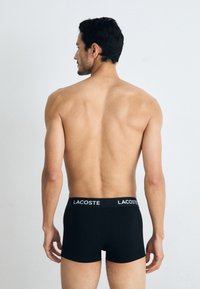 Black cotton boxer briefs with a white "LACOSTE" logo on the waistband, featuring a fitted design and mid-thigh length.