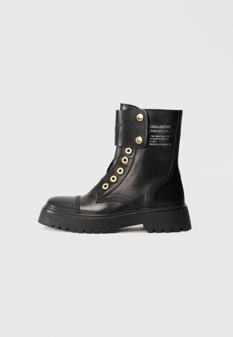 Black leather ankle boot featuring a chunky sole, gold hardware, and a flap with snap closure. Text branding on the side.