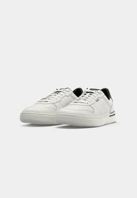 White leather sneakers with a smooth texture, rounded toe, black accents at the heel, and subtle striped detailing on the sole.
