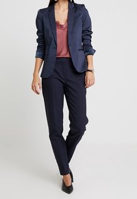 Marinblå kavaj med prickar och en skräddarsydd passform, lager på lager över en vinröd topp med spetskant. Matchas med marinblå slim fit-byxor och svarta klackar.