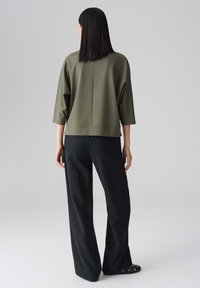 Olijfgroene, loszittende top met driekwart mouwen en een ronde zoom, gecombineerd met zwarte, wijde broek. Gladde textuur, minimalistisch ontwerp.