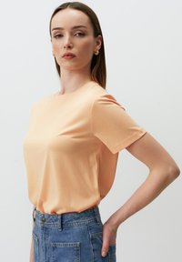 Różowopomarańczowa koszulka z krótkim rękawem, wykonana z miękkiego materiału, z klasycznym okrągłym dekoltem i luźnym krojem, zestawiona z szortami dżinsowymi o wysokim stanie.